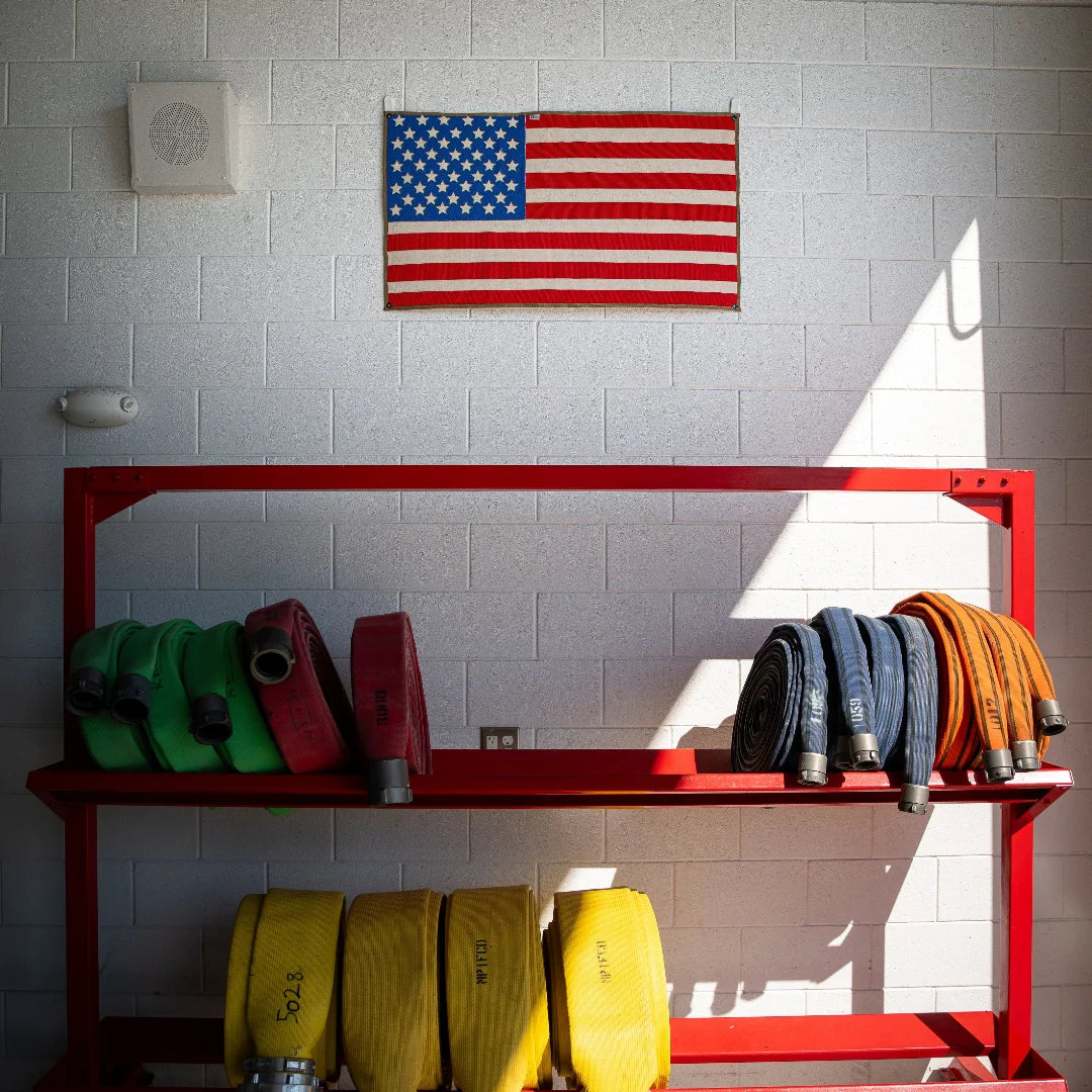 A large American flag by Recycled Firefighter handcrafted from decommissioned 5-inch fire hose with a Coyote Arid border and four brass mounting grommets.