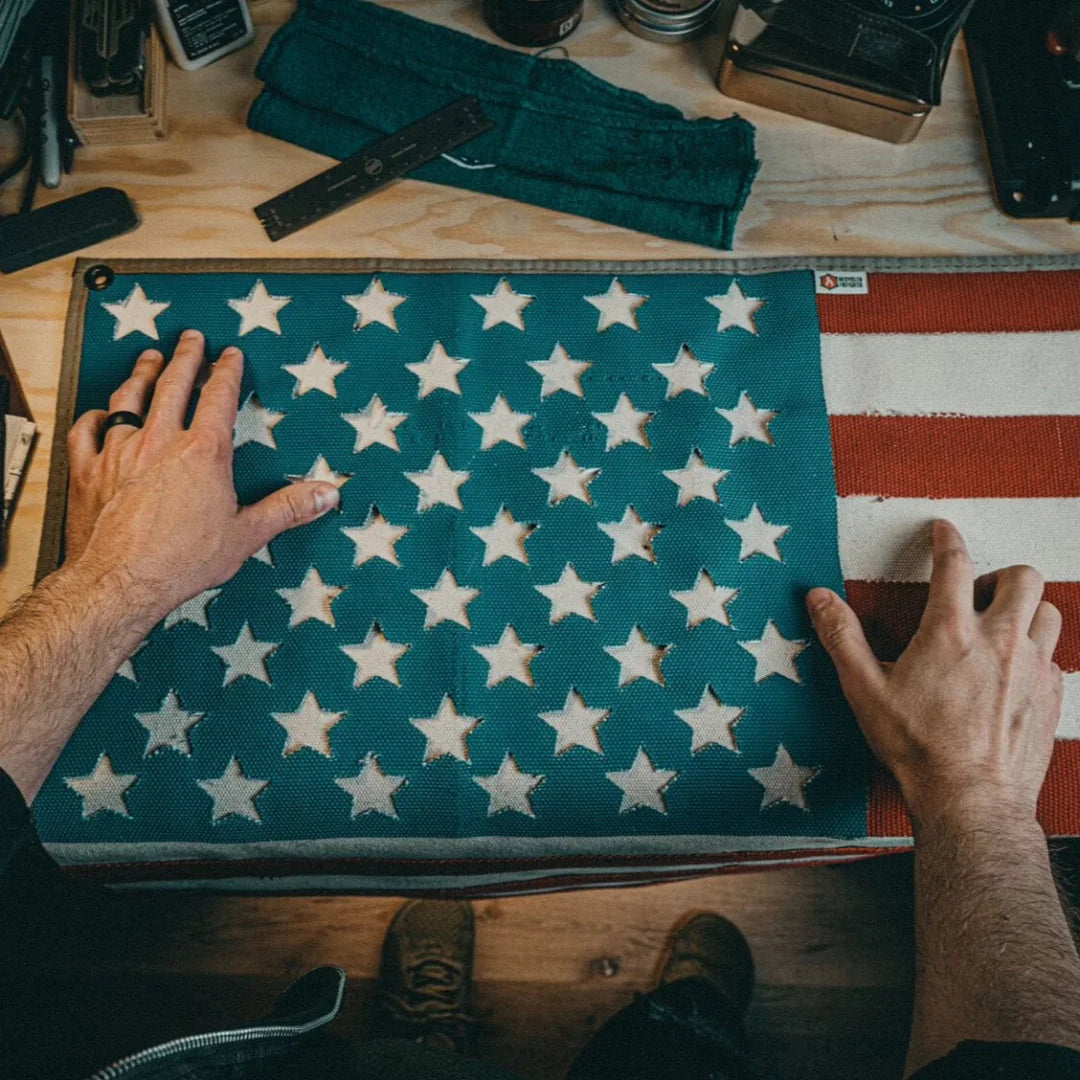A large American flag by Recycled Firefighter handcrafted from decommissioned 5-inch fire hose with a Coyote Arid border and four brass mounting grommets.