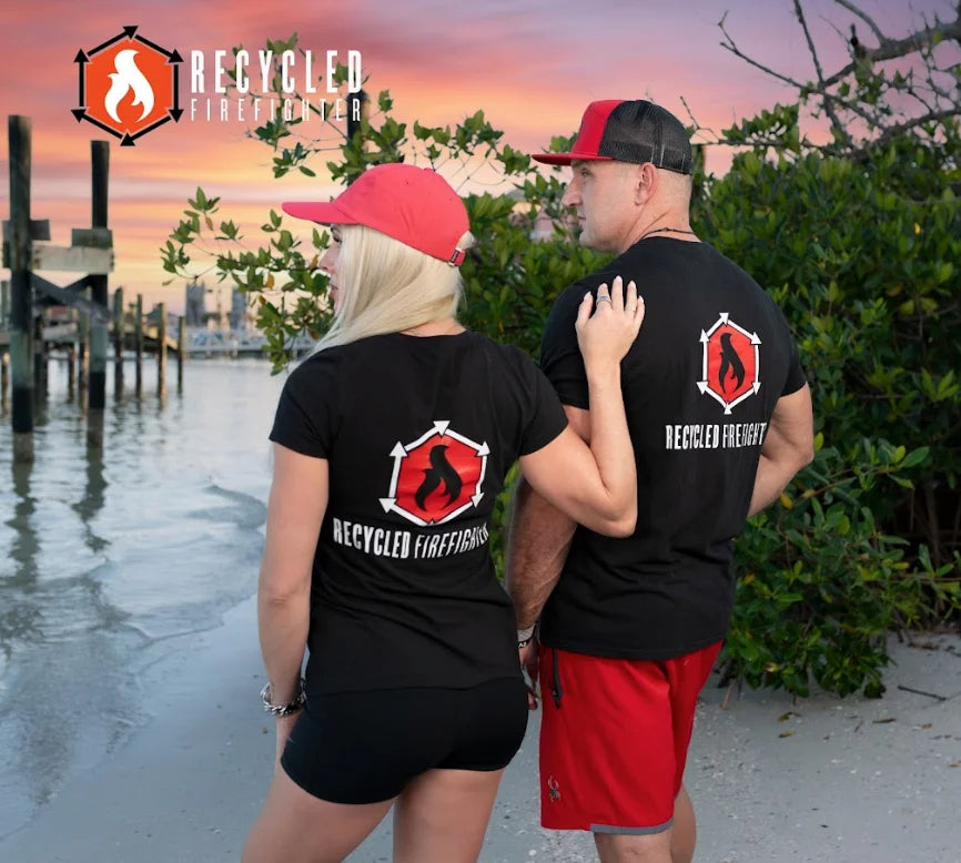 A soft, black t-shirt showing the Recycled Firefighter logo. The logo is a circular design with two crossed firefighting axes and the brand name in bold lettering. Available in men's crew neck and women's v-neck styles.