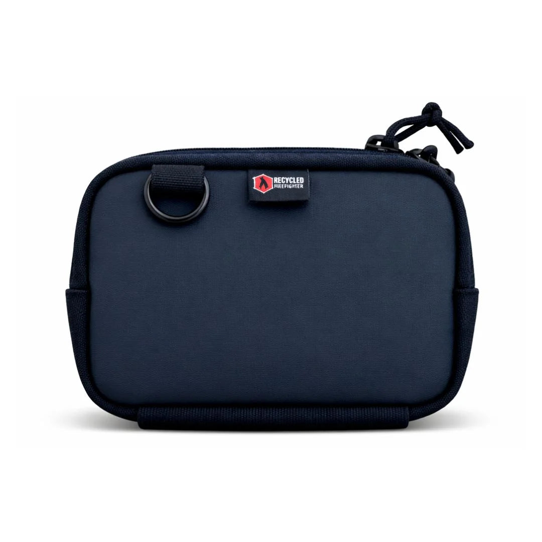 A Recycled Firefighter Trailhound fanny pack in Vintage Red firehose material. The fabric shows a weathered, authentic distress from years of service, featuring a matte red finish with a black zipper, black adjustable strap, and a side brass grommet for dog bags.