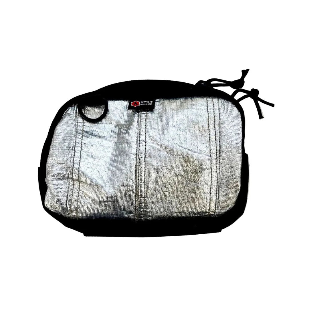 A unique silver bunker gear fanny pack by Recycled Firefighter made from heat-reflective aluminized firefighter material. The shimmering metallic silver body contrasts with the black zipper, side grommet, and elastic bottom pouch.