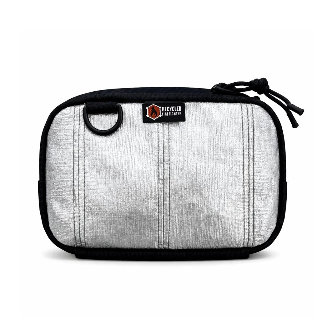 A unique silver bunker gear fanny pack by Recycled Firefighter made from heat-reflective aluminized firefighter material. The shimmering metallic silver body contrasts with the black zipper, side grommet, and elastic bottom pouch.