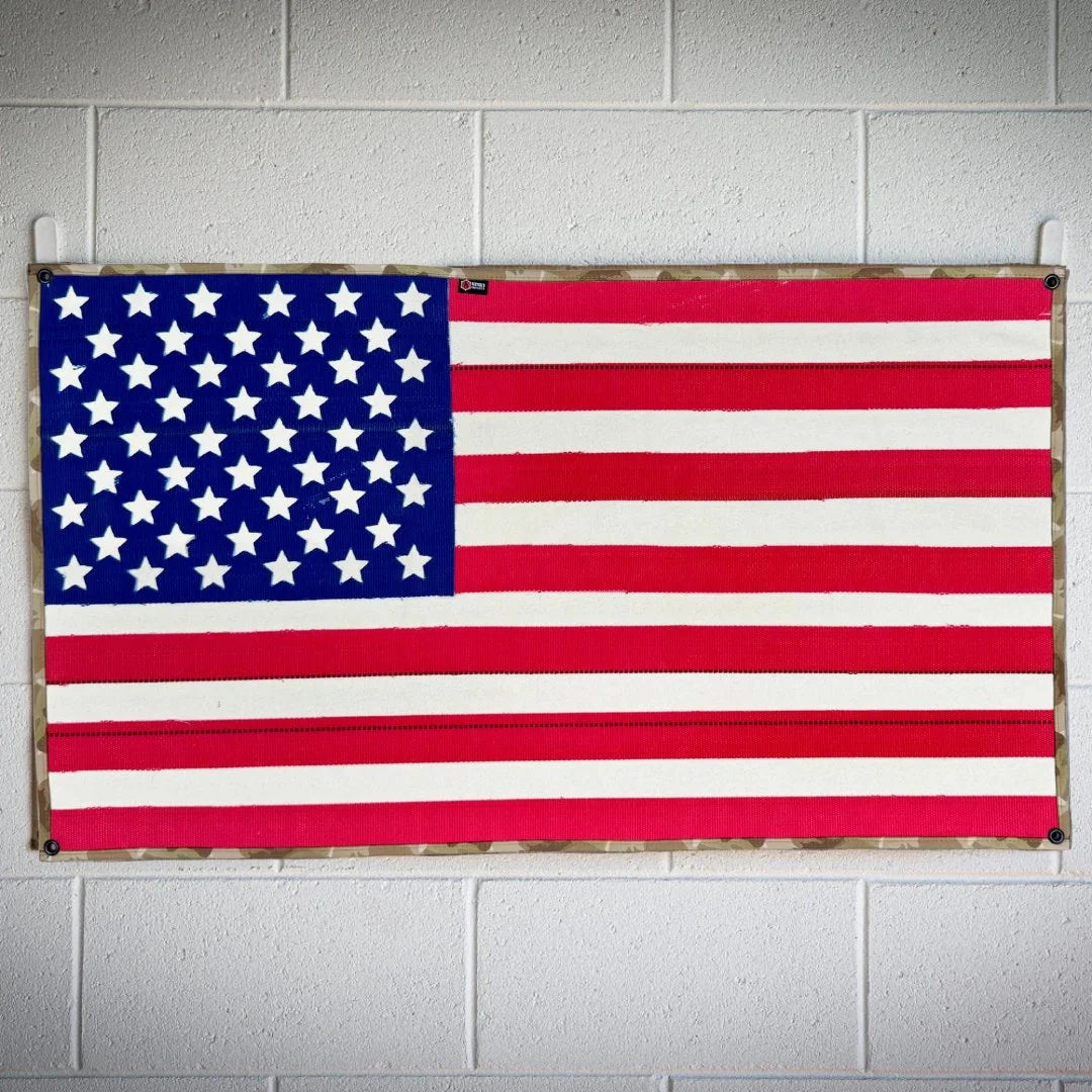 A large American flag by Recycled Firefighter handcrafted from decommissioned 5-inch fire hose with a Coyote Arid border and four brass mounting grommets.