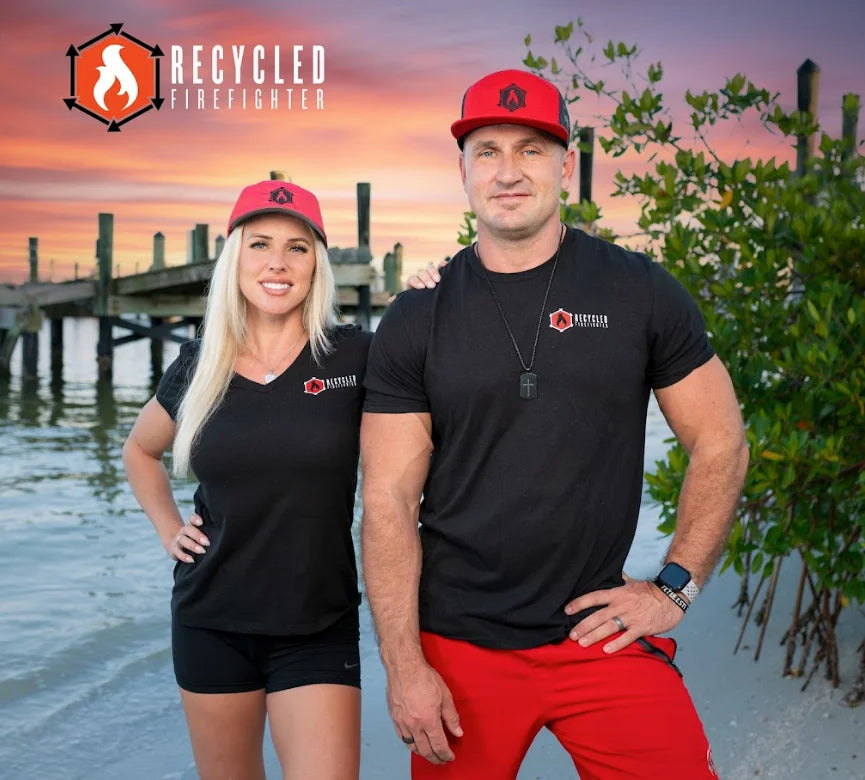 A soft, black t-shirt showing the Recycled Firefighter logo. The logo is a circular design with two crossed firefighting axes and the brand name in bold lettering. Available in men's crew neck and women's v-neck styles.