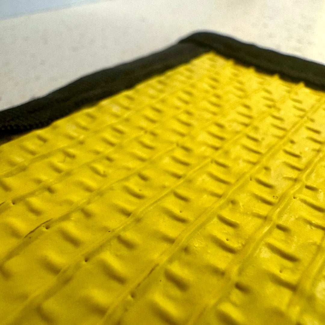 A heavy-duty Drop Zone Mat HD Attack Hose Edition made from repurposed yellow fire hose provides a durable, oil-resistant work surface for firearm maintenance and gear organization.