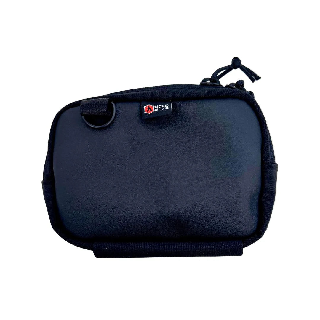 A rugged black leather fanny pack by Recycled Firefighter, crafted from durable boot-grade leather. The pack features a matte black finish with a visible natural grain, a heavy-duty black YKK zipper, and a black adjustable nylon strap. A brass grommet is visible on the side for dog waste bags.