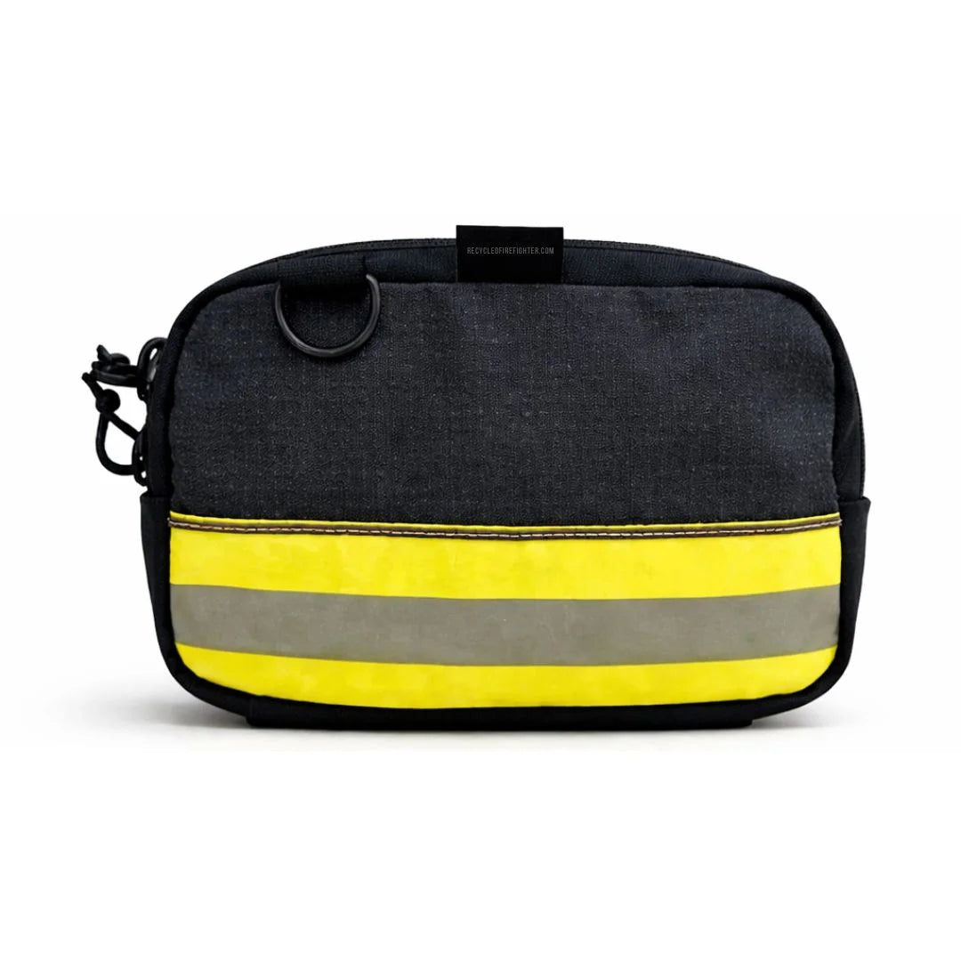 A black bunker gear fanny pack from Recycled Firefighter with a bold horizontal yellow and silver reflective stripe. The tactical-style bag includes a black adjustable waist strap and a brass side grommet for dog waste bags.