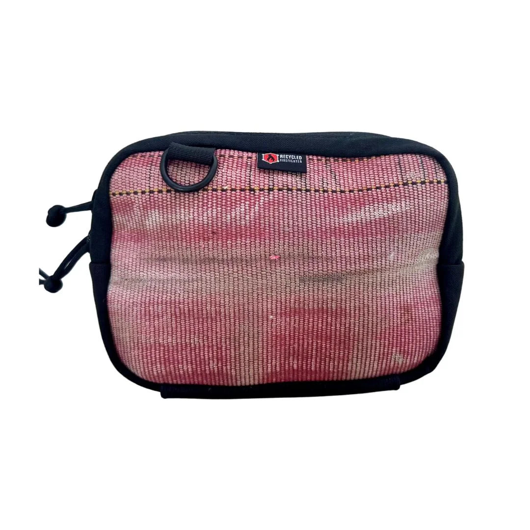 A Recycled Firefighter Trailhound fanny pack in Vintage Red firehose material. The fabric shows a weathered, authentic distress from years of service, featuring a matte red finish with a black zipper, black adjustable strap, and a side brass grommet for dog bags.